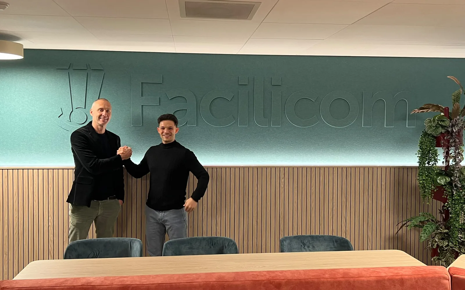 Koen Slinger geeft een collega van Facilicom een hand voor de Facilicom-wand in hun kantoor.